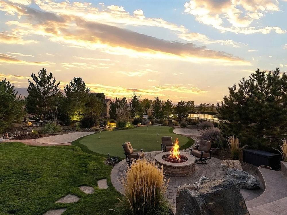 Round patio with a fire pit, lawn and ornamental grasses at sunset